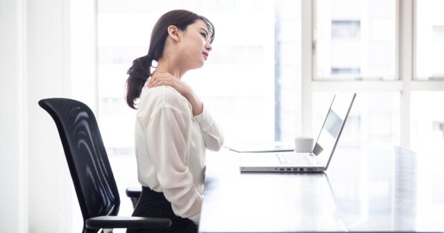 パソコンの前で椅子に座って肩が辛そうにしている女性